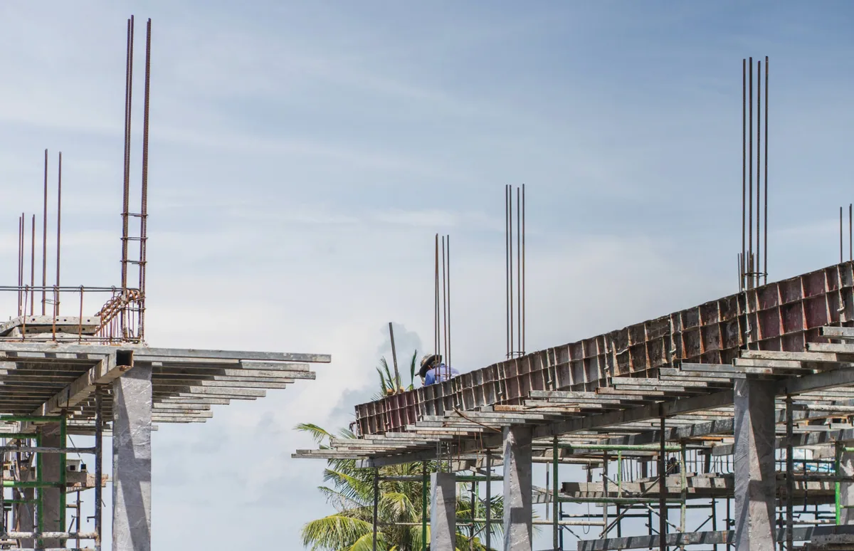 A concrete frame under construction, with steel rods rising from its columns against a pale sky
