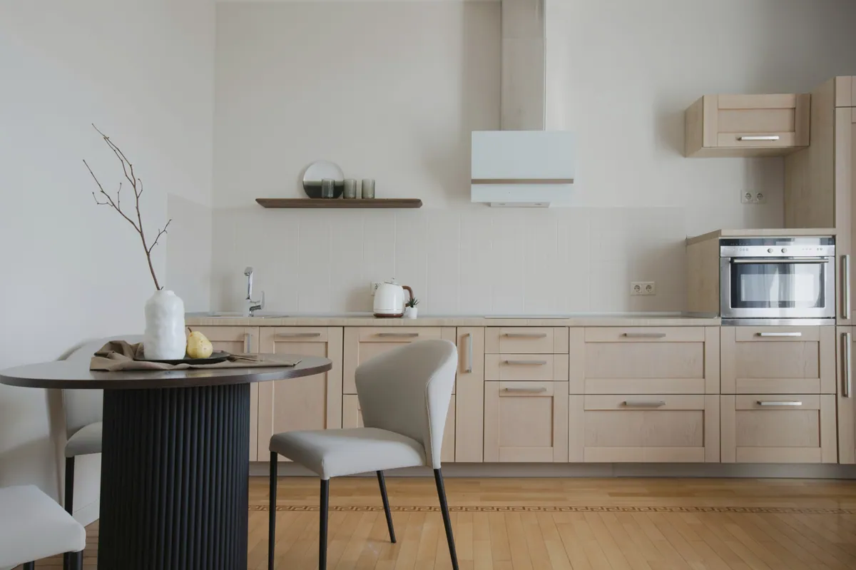 A calm kitchen with pale timber cabinets, a round dining table and soft daylight