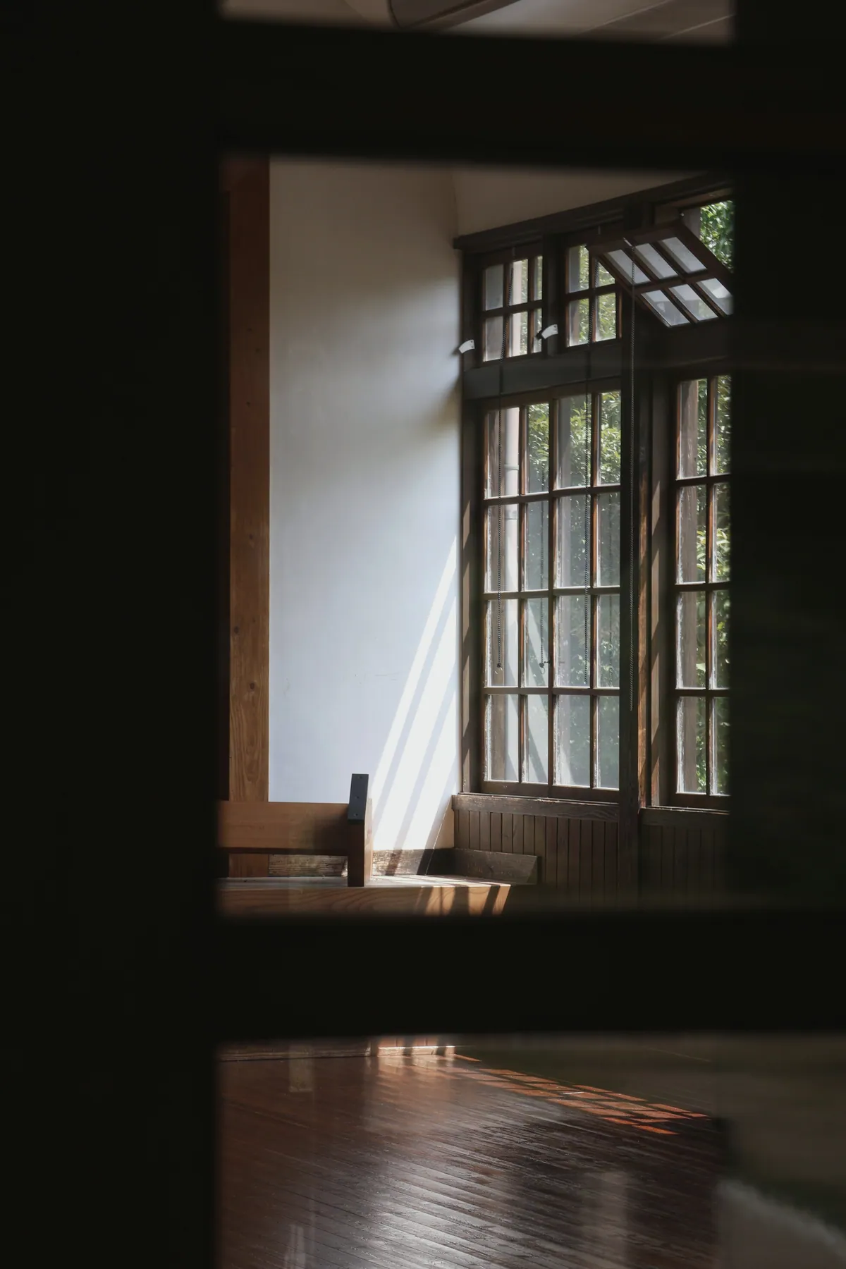 Sunlight through a tall timber-framed window falling across a polished wooden floor